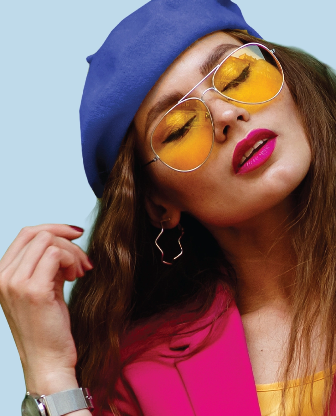 Woman wearing silver aviator sunglasses with yellow lenses, a blue beret, and a pink blazer against a light blue background.