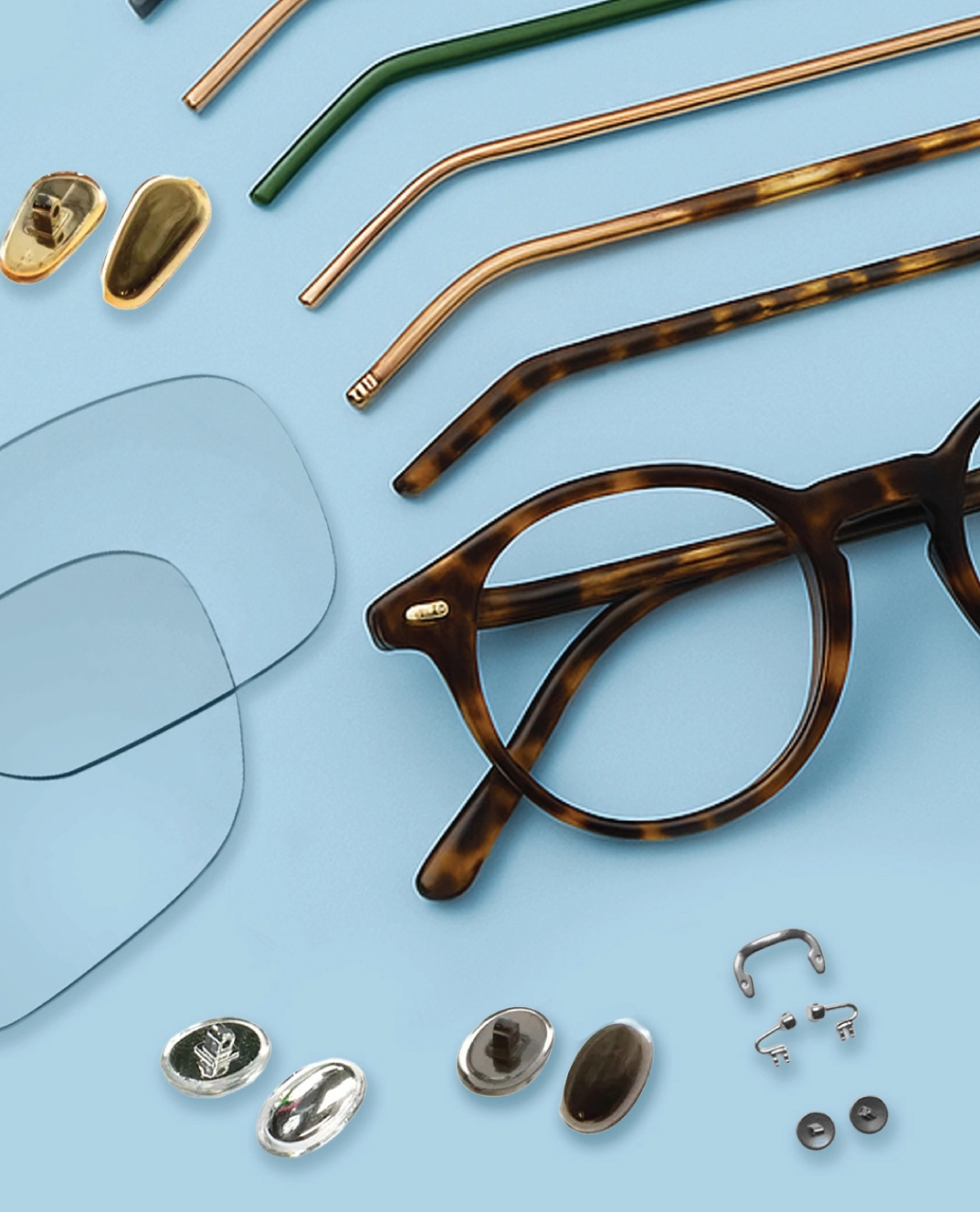 Disassembled eyeglasses on a light blue surface—temples, lenses, nose pads, screws, and frame pieces arranged neatly.
